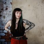 Chlo Eve, tattoo artist from Leeds, standing against a brick wall