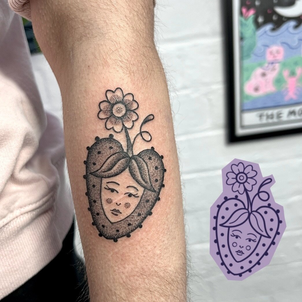 One of Gem Hawk's flash designs next to the finished tattoo, a strawberry with a face